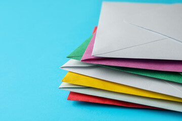 Stack of colorful paper envelopes on light blue background, closeup. Space for text