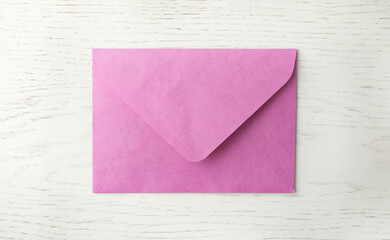 Pink paper envelope on white wooden background, top view