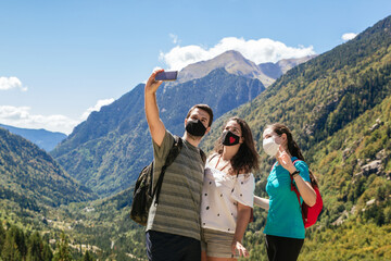 Stock photo of three friends wearing masks and taking a selfie while enjoying the mountain