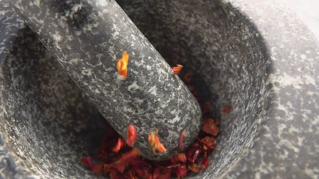 Pieces of red smoked tomato are falling into the stone mortar in slow motion