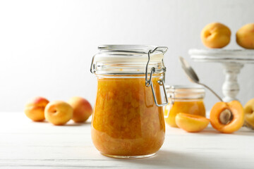 Jar of apricot jam and fresh fruits on white wooden table