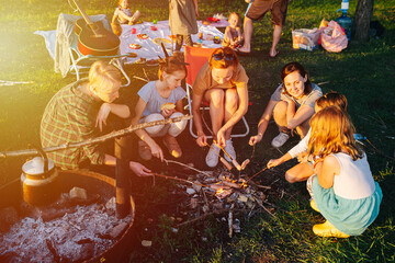 People sitting in a tight circle around bonfire, cooking sausages