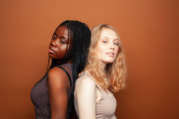 young pretty caucasian, afro woman posing cheerful together on brown background, lifestyle diverse nationality people concept