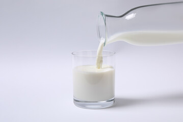 Pouring milk into glass on white background