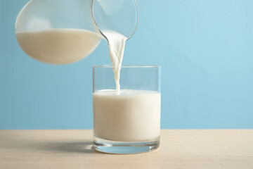 Pouring milk into glass on wooden table against light blue background