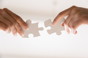 Close up of people assemble jigsaw puzzle find business solution or perfect match. Diverse employees workers put join pieces, participate in teambuilding activity. Teamwork, collaboration concept.
