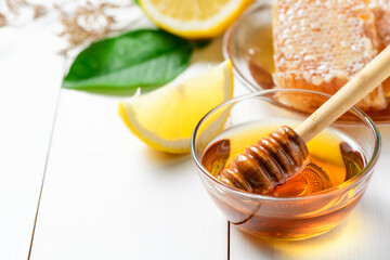 Honey with wooden honey dipper in bowl with sliced lemon