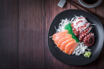 Salmon and Tako sashimi on black dish with chopsticks