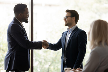 Smiling businessman handshake male colleague congratulate with job promotion or work success. Happy diverse business partners shake hands get acquainted greeting or close deal at meeting in office.