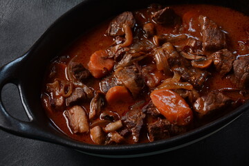Beef Bourguignon in a pan. Stew with red wine ,carrots, onions, garlic, a bouquet garni, and garnished with pearl onions, mushrooms and bacon. French cuisine- regional recipe from Burgundy