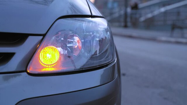 Car is parked on the side of highway, turn signal flashes indicating drivers intention to make u-turn or go on road, close up. Automobile turned on emergency light after accident, waiting for help.
