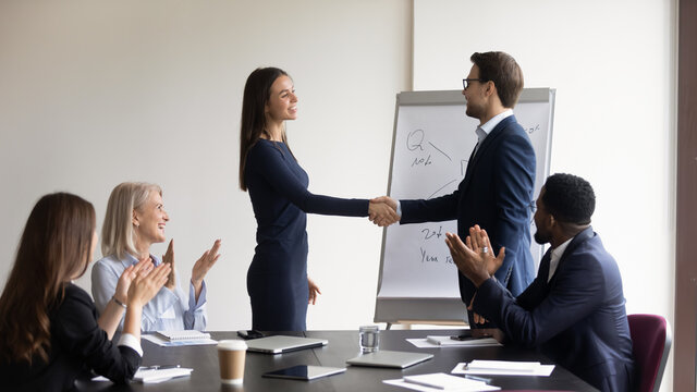 Motivated diverse businesspeople shake hands get acquainted greeting at team meeting in office. Smiling business partners handshake close deal or make agreement at briefing. Partnership concept.