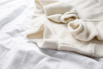 Fototapeta na wymiar Warm fleece sweater on white crumpled fabric, closeup