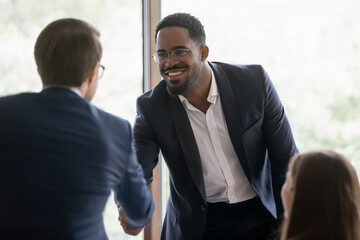 Happy diverse businessmen shake hands greeting get acquainted at business meeting in office. Smiling multiracial male partners or colleagues handshake close deal after successful negotiation.