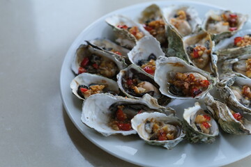 close up a plate of grilled oysters with spice on white table.