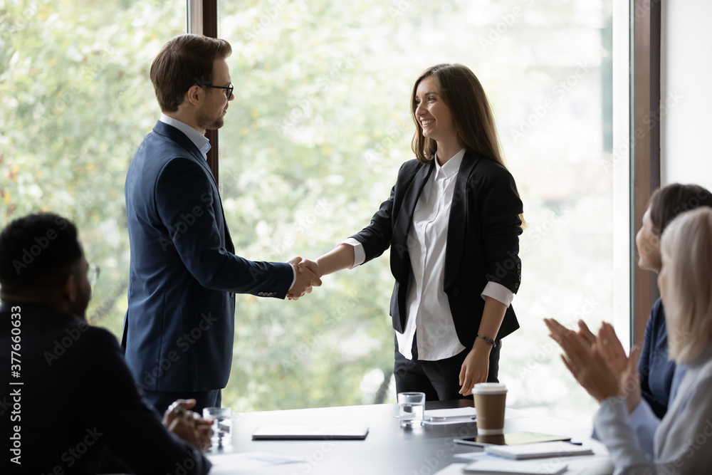 Canvas Prints Young businessman handshake happy female colleague or employee congratulate with job success. Smiling diverse businesspeople shake hands get acquainted greeting at office meeting. Cooperation concept.