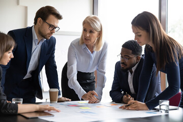 Concentrated diverse businesspeople talk brainstorm at team meeting discussing paperwork together....