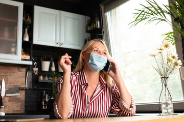 Woman in quarantine wearing protective mask and smart working in home kitchen.