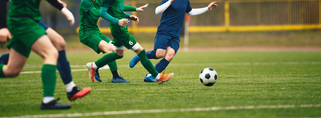 Teenagers in soccer duel. Boys in two football teams running after classic soccer ball. Horizntal sports background. Legs of young players on football pitch