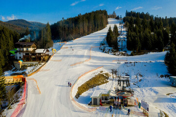 Aerial view of landscape of ski and snowboard slopes through pine trees going down to winter resort in Carpathians