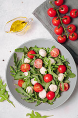 Diet and healthy salad with arugula, cherry tomatoes, mozzarella cheese and olive oil on white background