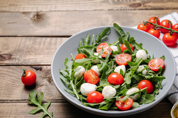 Diet and healthy salad with arugula, cherry tomatoes, mozzarella cheese and olive oil on wooden background