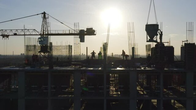 Silhouettes of builders (workers) on the rooftop of a residential building under construction (in a course of building)