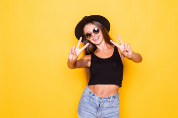 Young woman showing peace gesture standing isolated over yellow background .