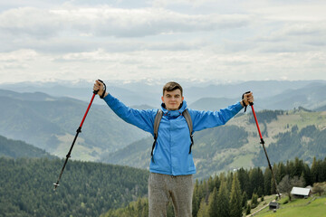 A mountain climber is high in the mountains against the sky, celebrating the victory, raising his...