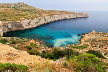 Fototapeta na wymiar Incredible colors of view on colorful rocks on coastline in Malta. Juicy blue and green sea, blue sky. Beautiful landscapce. Hiking way on cliffs. Unforgettable scenery.