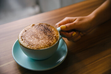 Women hand holding coffee cup with hot cappuccino on the wooden table.