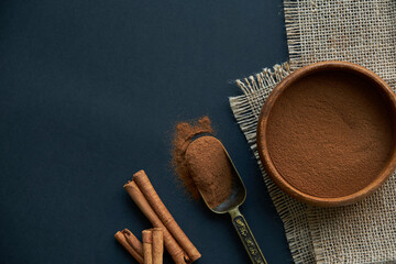 cinnamon sticks, tied with jute rope in rustic style. Ground cinnamon in a wooden bowl and vintage scoop. Close up on a black background. copy space for text. Top view, flat lay.