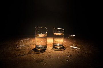 Broken glasses on wooden table at dark toned background with fog. Selective focus