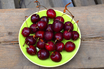 Ripe cherries in a green plate. On a wooden background. Tasty. Close-up