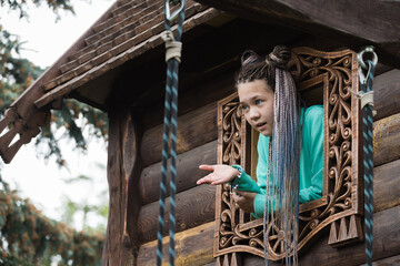 Beautiful girl with dreadlocks on her head plays in the playground in large wooden house.