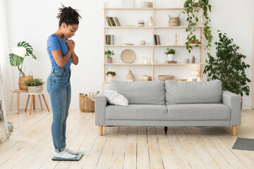 Happy African Girl Weighing Herself Standing On Weight-Scales At Home