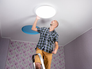 A man with a stepladder sets the ceiling lamp in the room.