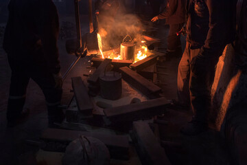 The workers are pouring molten metal to molds for casting. Casting is a manufacturing process in which a liquid material is usually poured into a mold.