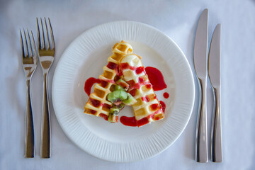 Waffles with red berry Compote and sliced kiwi on a white plate on a white table cloth 