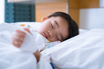 Asian cute little boy is sleeping on the sickbed with saline intravenous on hand. and the face with tears in the patient room in hospital selective focus.  Healthcare medical and people concept.