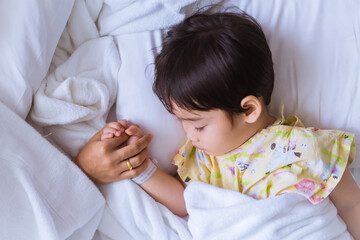 Hands of mother and sick Asian little boy holding together to give encouragement, little boy sleeping on sickbed in hospital. Healthcare medical and people concept.
