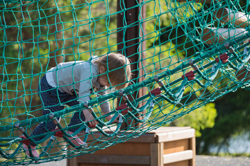 Small child plays on playground crawling in rope net.