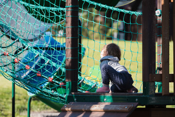 Small child plays on playground crawling in rope net.