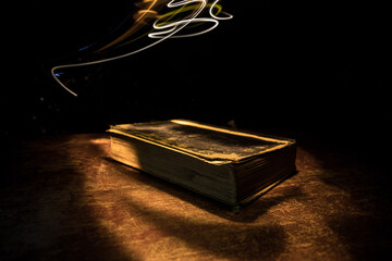 Imagine a picture book of an ancient book opened on a wooden table with a sparkling golden background. With magical power. magic. lightning around a glowing glowing book In the room of darkness