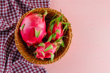 Dragon fruit in a wicker basket on pink and picnic cloth background, flat lay.