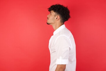 Young arab man with afro hair wearing shirt standing over isolated red background looking to side, relax profile pose with natural face with confident smile.