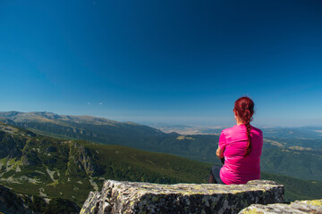 Naklejka premium Young lady enjoying the scenery on the top of a mountain peak.