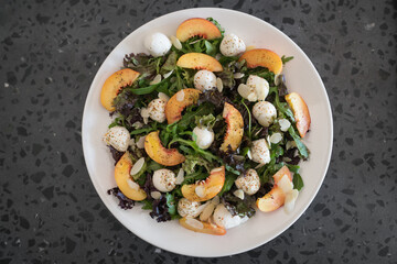 Top view of salad with nectarines, mozzarella and mixed greens in white plate on concrete background