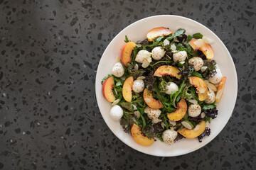 Top view of salad with nectarines, mozzarella and mixed greens in white plate on concrete background