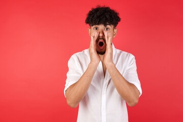 Fototapeta na wymiar Young arab man with afro hair wearing shirt standing over isolated red background, shouting excited to front.
